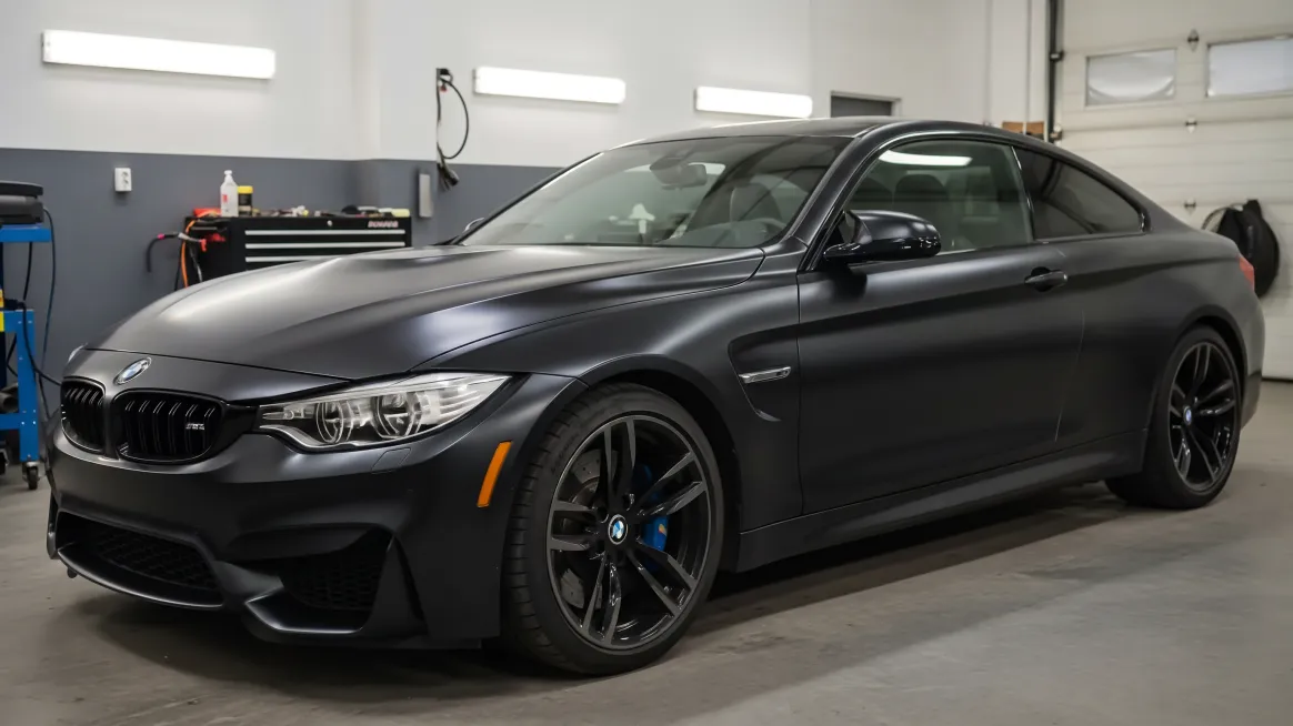 The same BMW M4 in the same workshop, wrapped in satin black